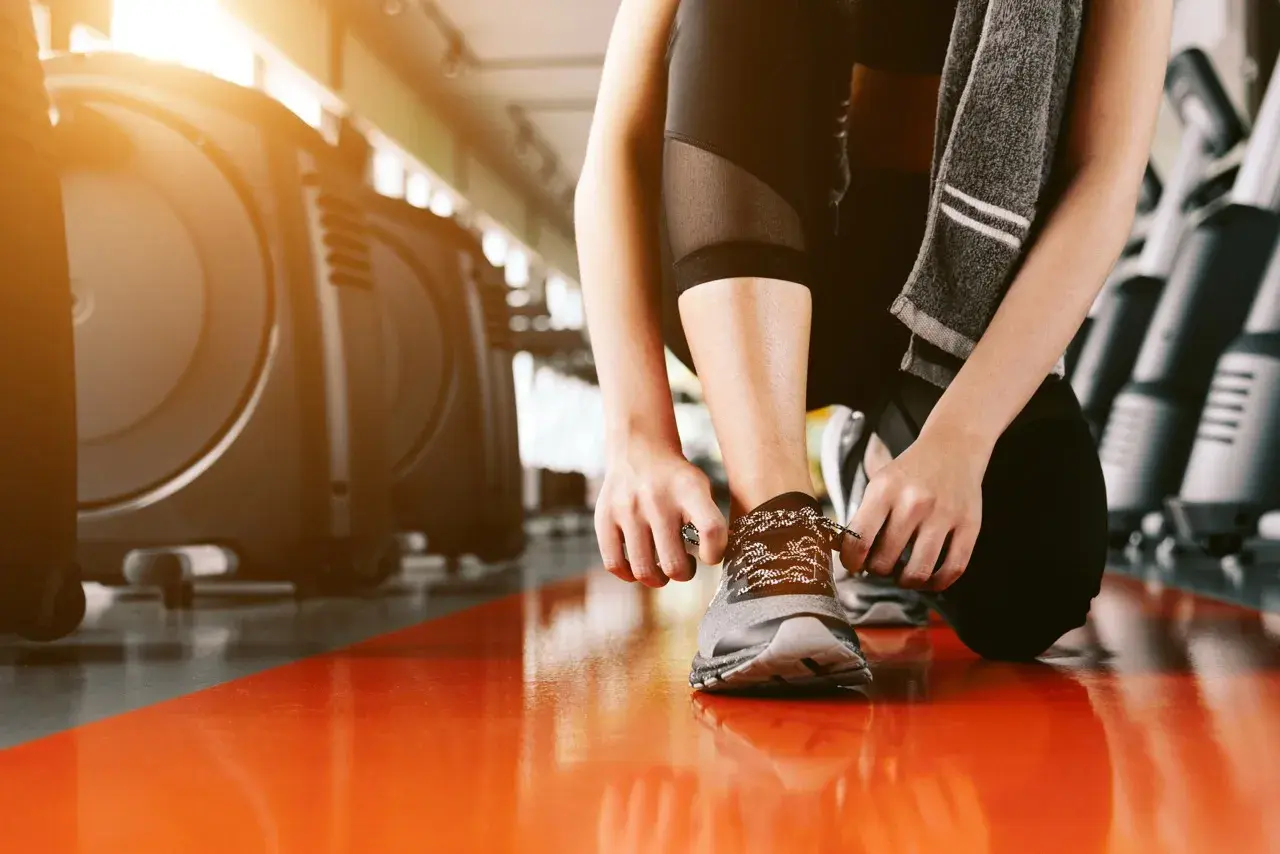 Donna si allaccia le scarpe in palestra, pronta per la corsa.