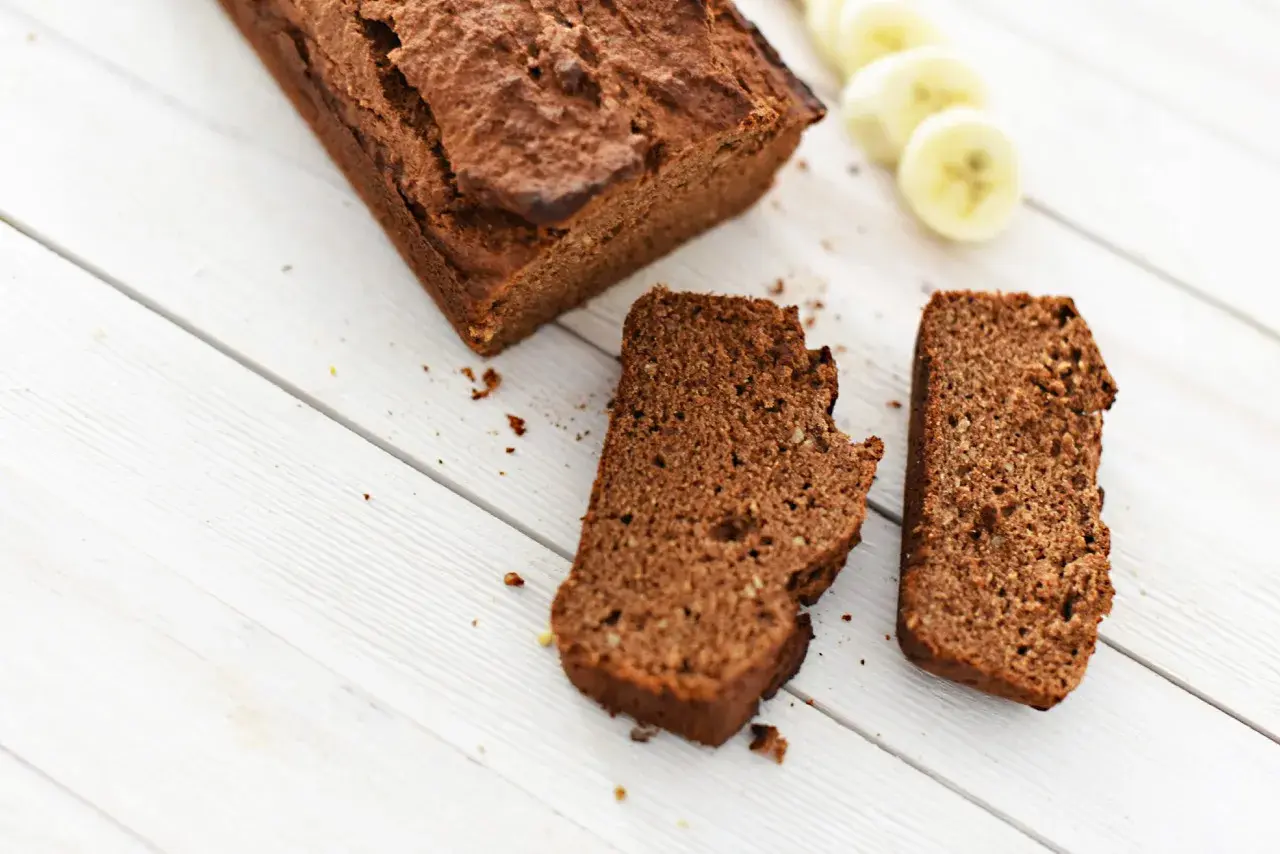 Chlebek bananowy Ani gotuje się na białych deskach. Obok leżą dwa kawałki ciasta i plasterki banana.