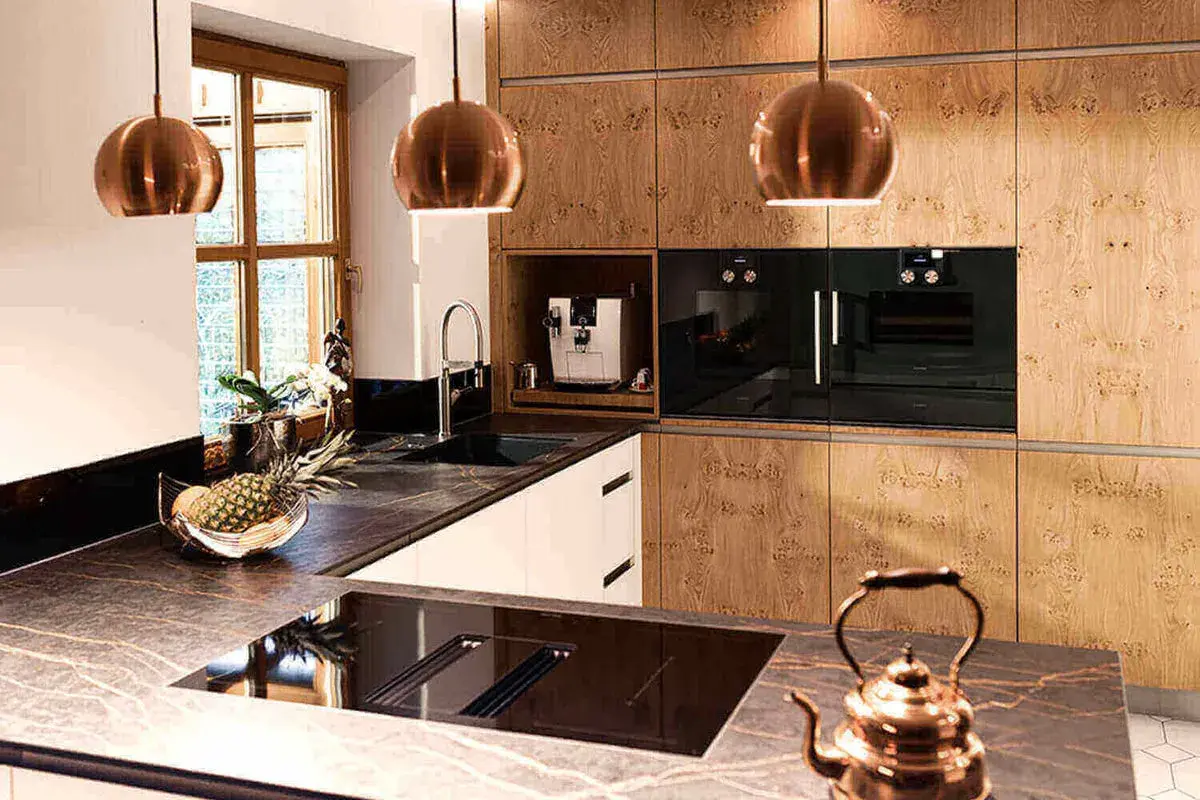 Elegante aplique de cocina con lámparas cobre, encimeras de mármol y electrodomésticos integrados.