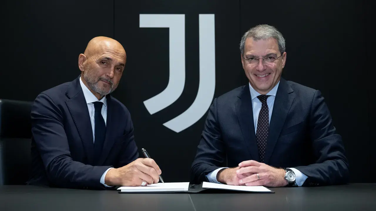 Dwóch mężczyzn w garniturach, prawdopodobnie trenerzy Juventusu, siedzi przy stole. Jeden z nich podpisuje dokumenty.
