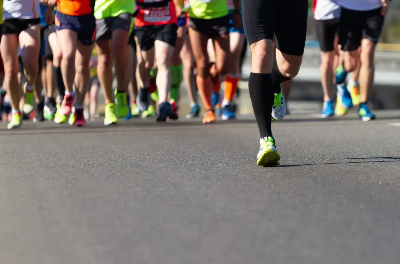 Gambe di corridori in maratona, con scarpe colorate. Un esempio di tabella maratona 4 allenamenti settimanali.