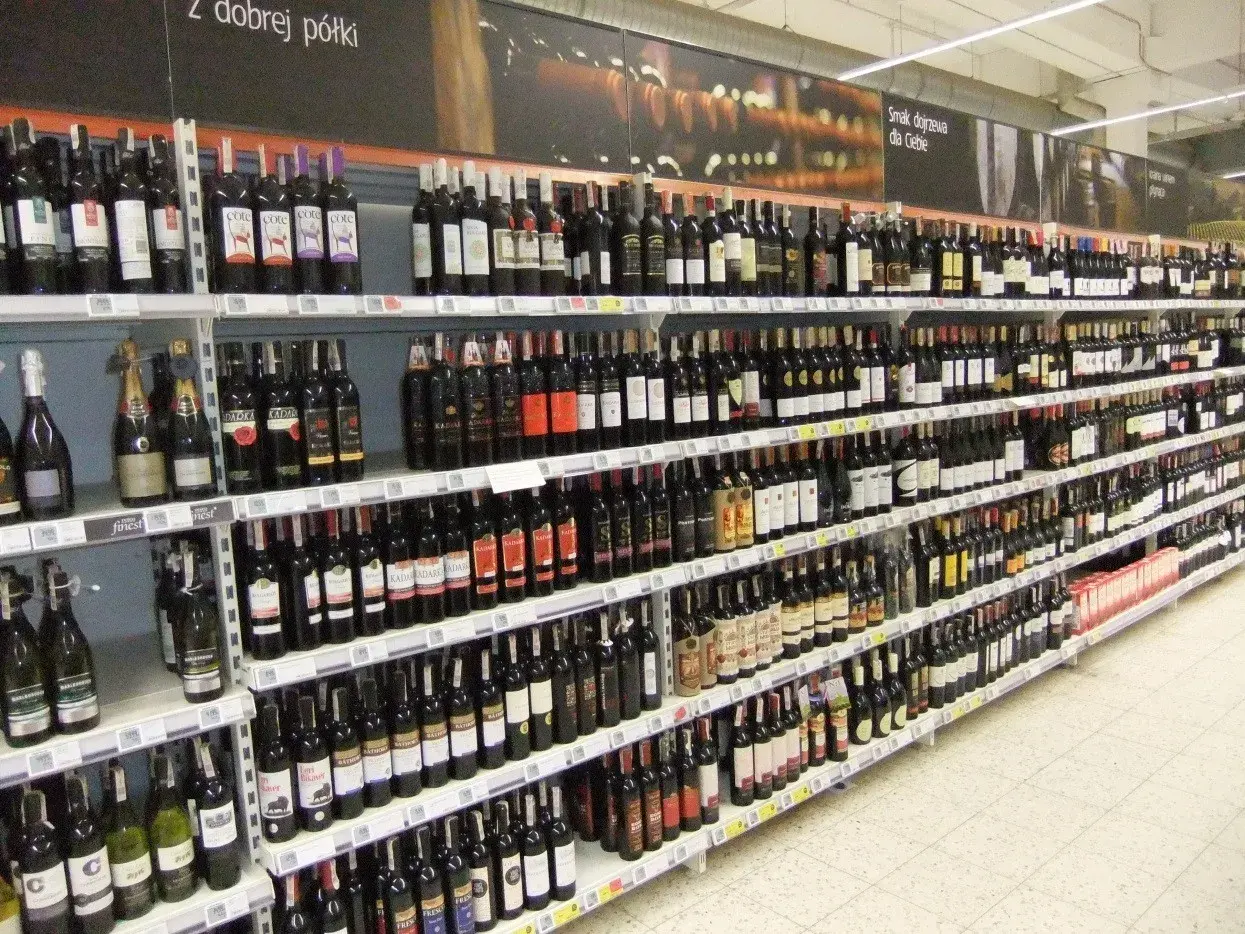 Rzędy butelek wina, w tym wino z suszonych winogron, na półkach sklepowych.