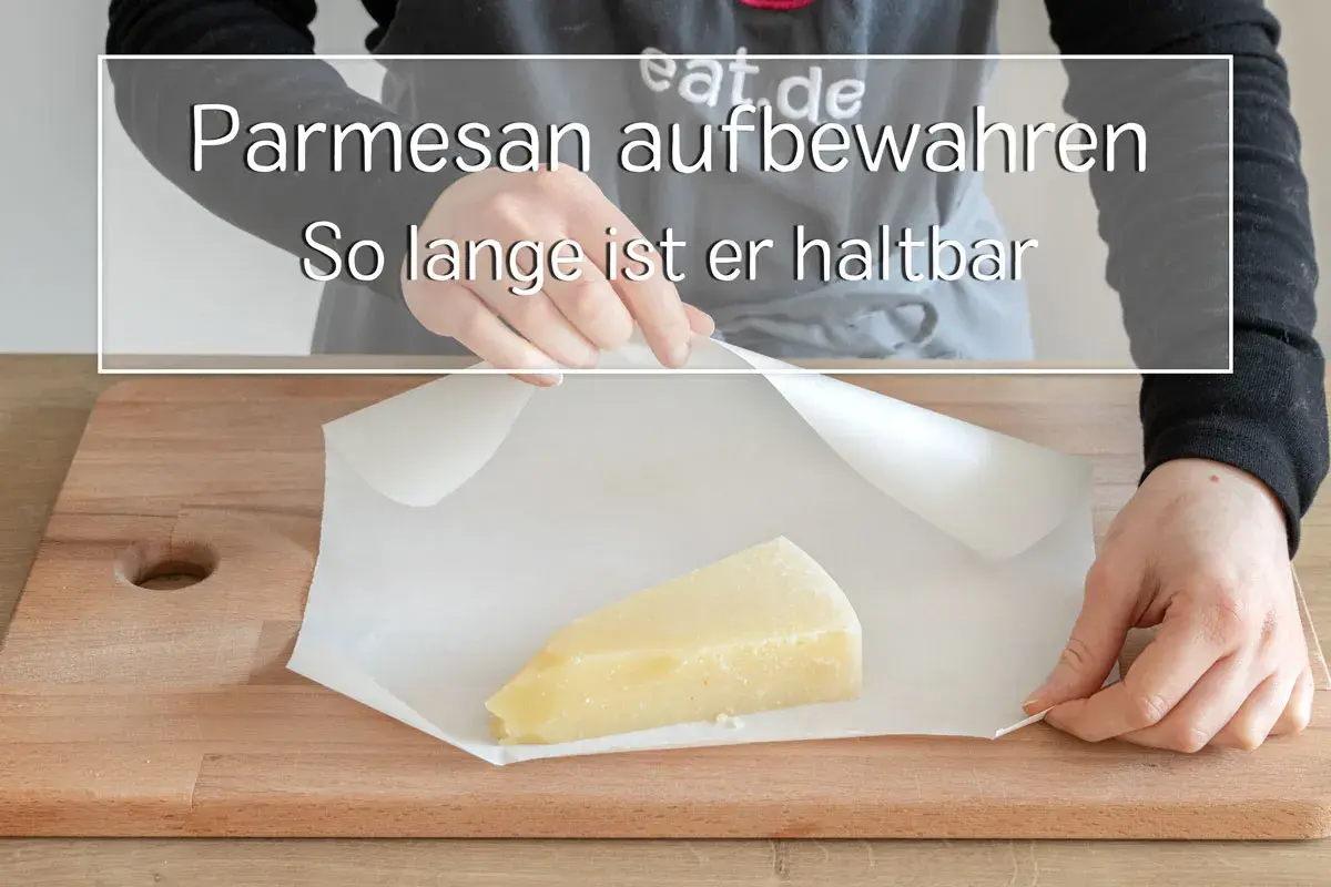 Ein Stück Parmesan wird auf Backpapier auf einem Holzbrett gelegt.
