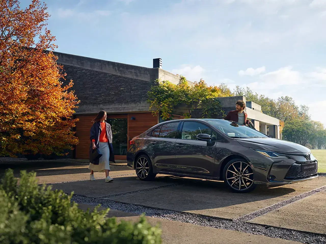 Un hombre y una mujer junto a un Toyota Corolla oscuro frente a una casa moderna.