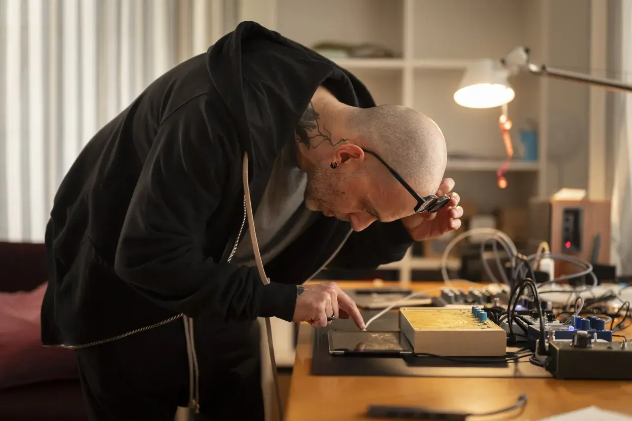 Mann mit Tattoos, der an einem Tisch mit elektronischen Geräten arbeitet, inspiriert von russischem Konstruktivismus.