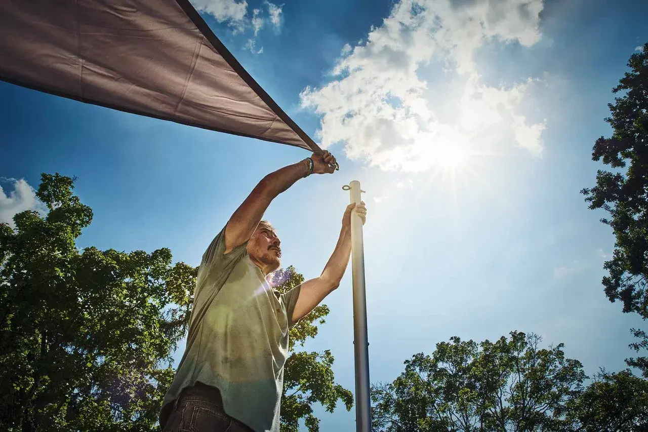 Man sätter upp ett solsegel mot en klarblå himmel med solens strålar som lyser.