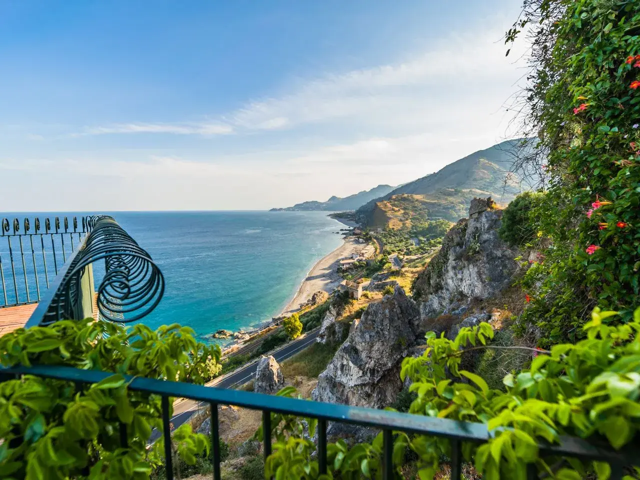Balkonblick auf Siziliens Küste: Türkises Meer, felsige Hänge & blühende Pflanzen. Perfekt für Sizilien Urlaub Tipps!