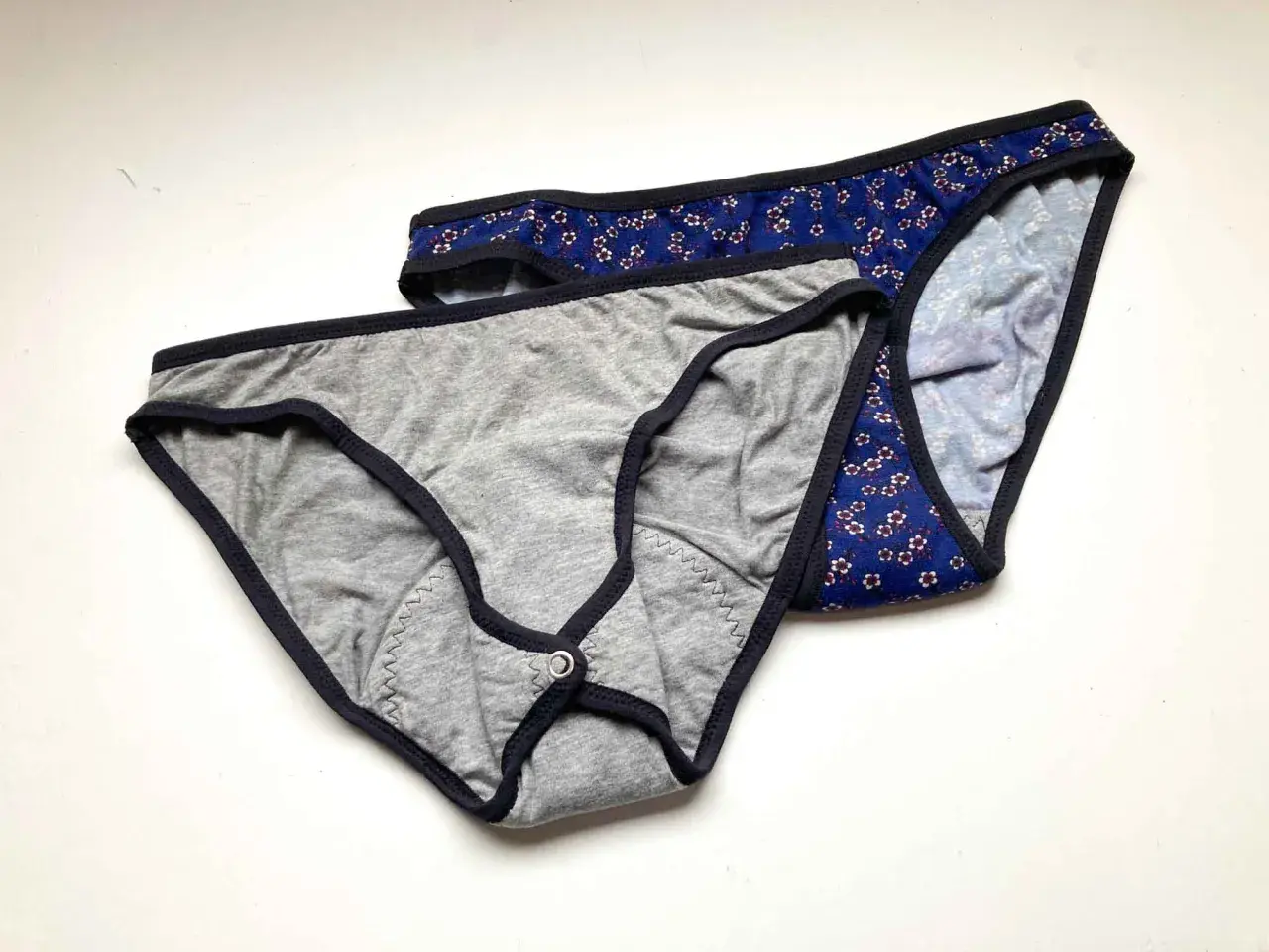 Two pairs of cotton underwear, one grey with a snap closure, the other blue floral. Perfect for a DIY period underwear project.