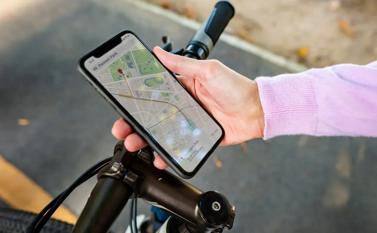 Dłoń trzyma smartfon z mapą, wskazującą trasę rowerową. Telefon pełni rolę licznika na rower, pokazując drogę do celu.