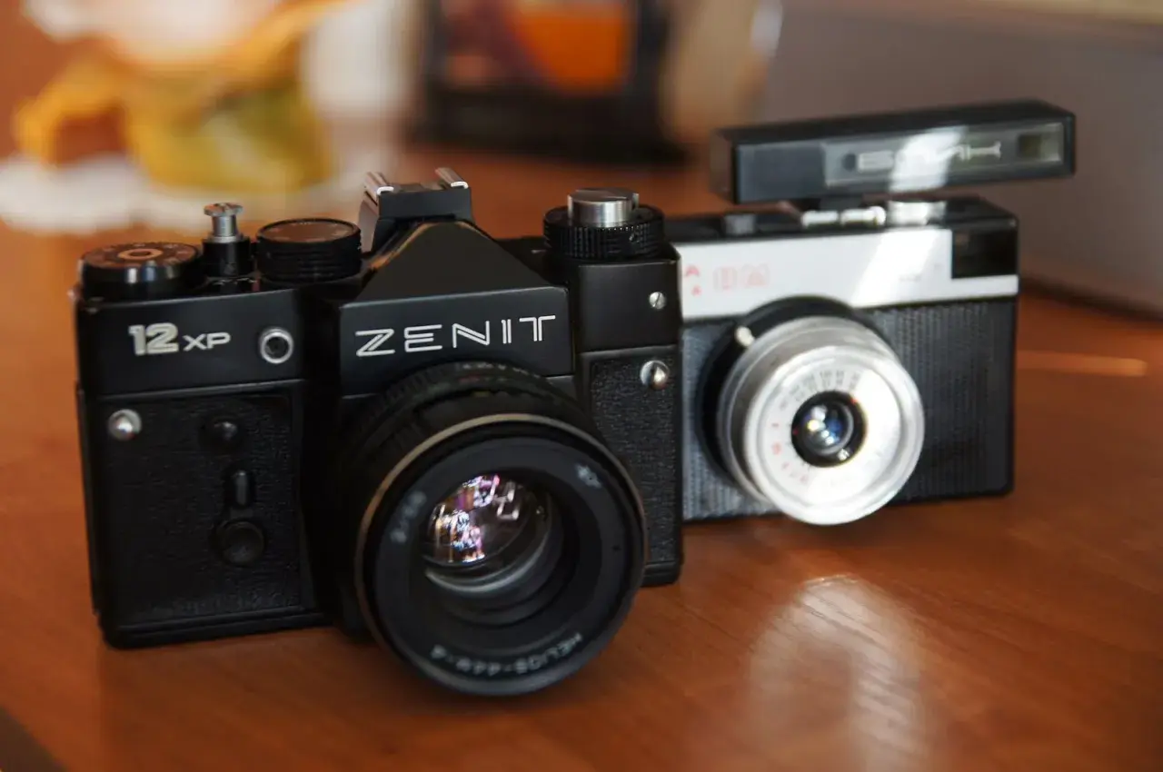 Dwa klasyczne aparaty na film: czarny Zenit 12XP i srebrno-czarny Smiena z lampą błyskową.