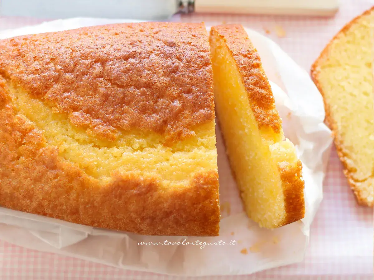 Un soffice plumcake allo yogurt, dorato e invitante, tagliato a fette su carta bianca.