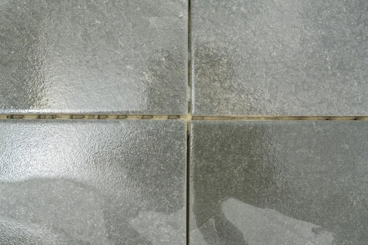 Dettaglio di quattro piastrelle grigie con fughe vuote, pronte per essere riempite. Una guida visiva su come riempire le fughe delle piastrelle.