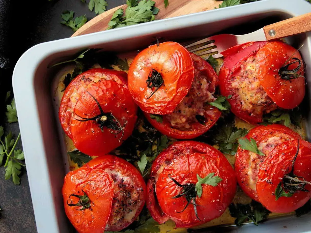 Six tomates farcies dorées, garnies d'une farce savoureuse et parsemées de persil frais, dans un plat de cuisson.