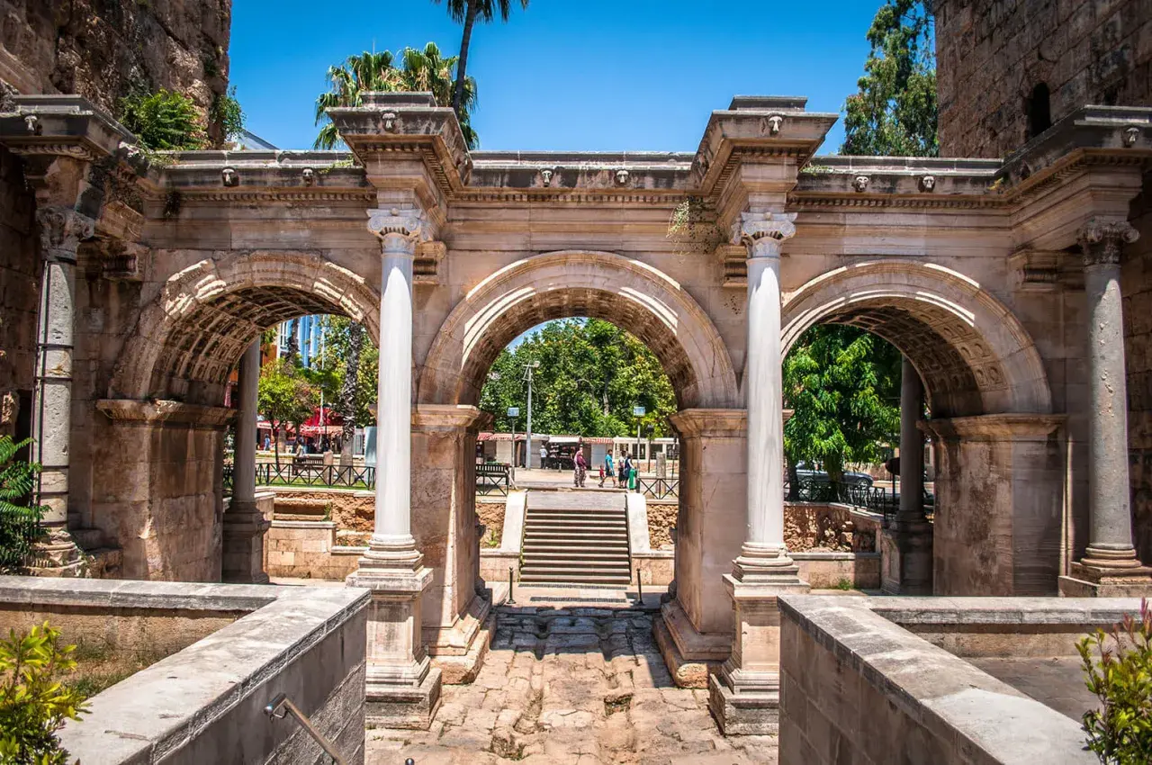 Łuk Hadriana, brama do **Antalya stare miasto**. Kamienne łuki i kolumny, w tle schody i zielone drzewa.