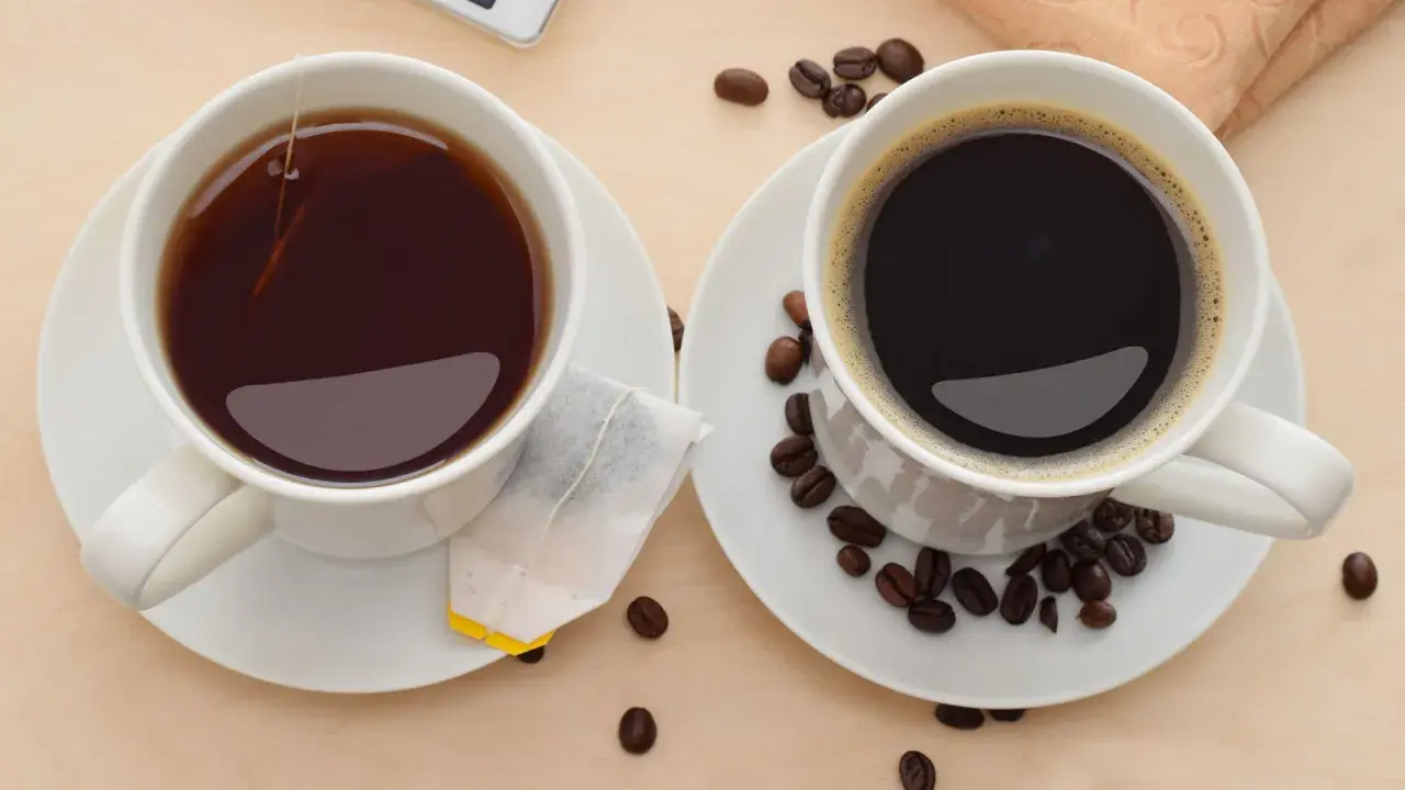 Zwei Tassen, eine mit schwarzem Tee und Teebeutel, die andere mit Kaffee und Kaffeebohnen. Perfekt, um Kaffee und Tee zusammen zu trinken.