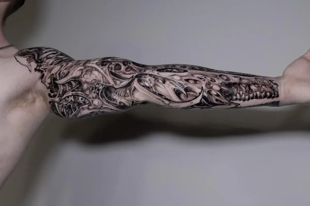 Imponujący greywash tattoo na ramieniu, przypominający mechaniczną protezę z ostrymi elementami i detalami.