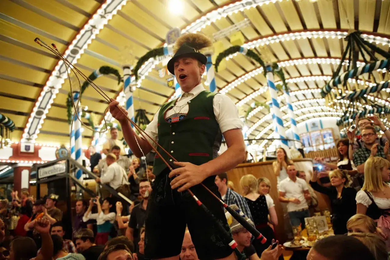 Mann im bierzelt oktoberfest mit Peitsche, jubelnde Menge im Hintergrund.