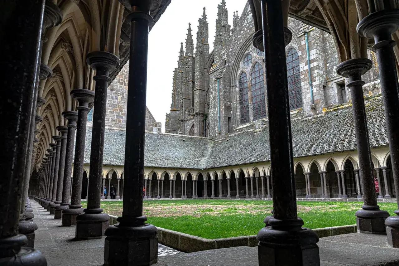 Ein Blick durch die Säulenhalle auf den Kreuzgang des Mont Saint Michel innen. Grüne Wiese und gotische Architektur.