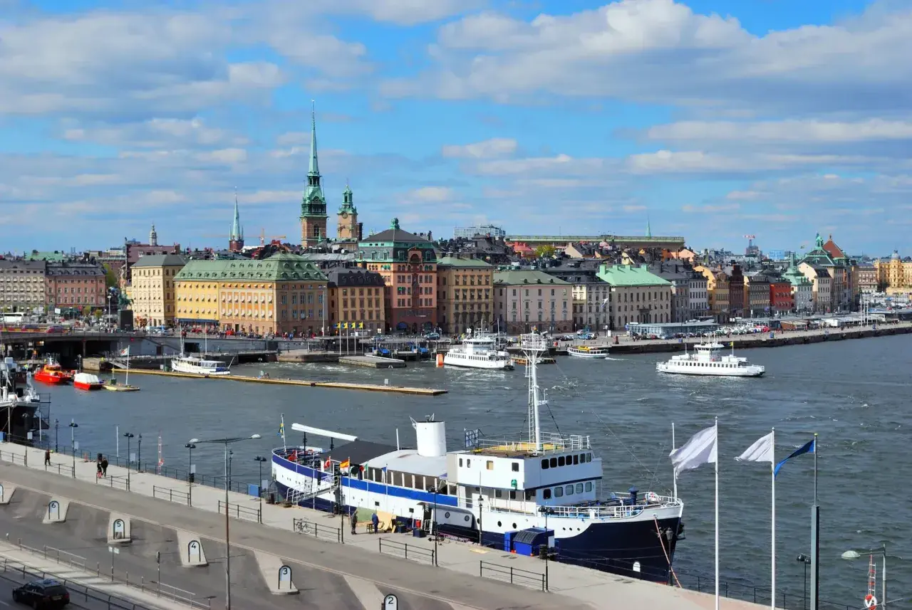 Widok na port w Sztokholmie, gdzie cumuje prom. W tle kolorowe kamienice i wieże.