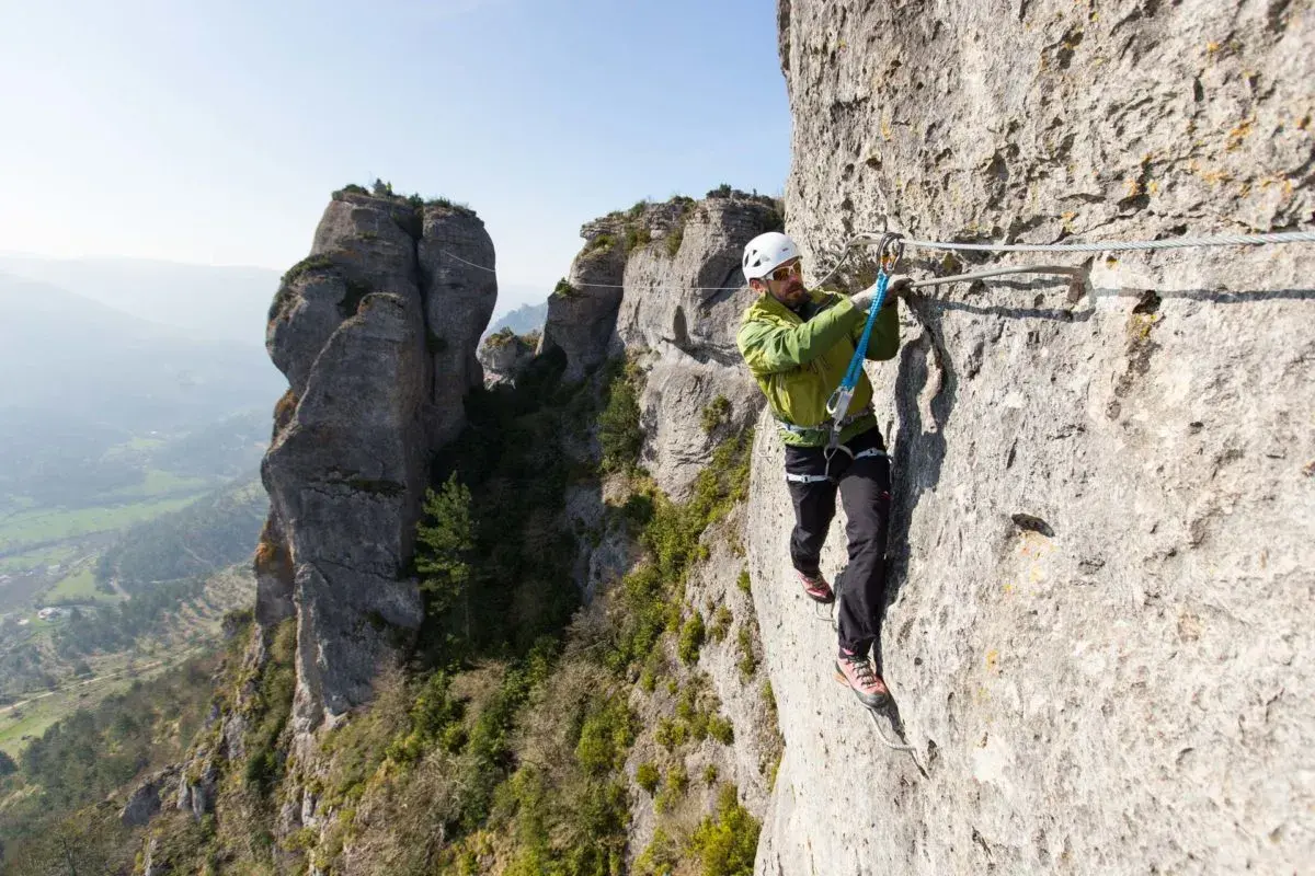 Un homme équipé pour la via ferrata progresse sur une paroi rocheuse, profitant d'un paysage spectaculaire.