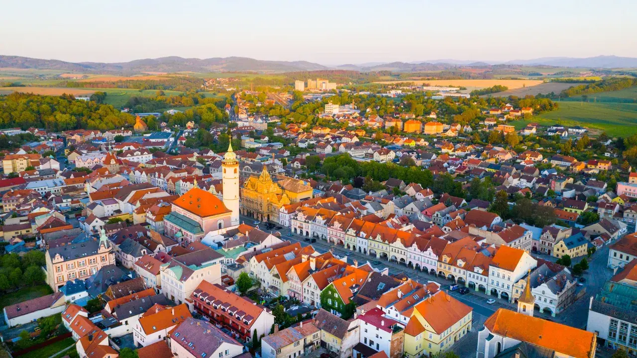 Luftaufnahme eines malerischen **Taus Tschechien** mit roten Dächern, einer Kirche und grünen Hügeln im Hintergrund.
