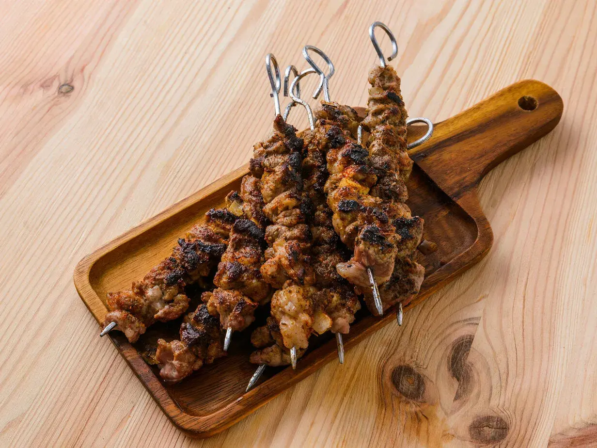 Cinq brochettes d'agneau grillées, savoureuses et légèrement caramélisées, reposent sur un plateau en bois.