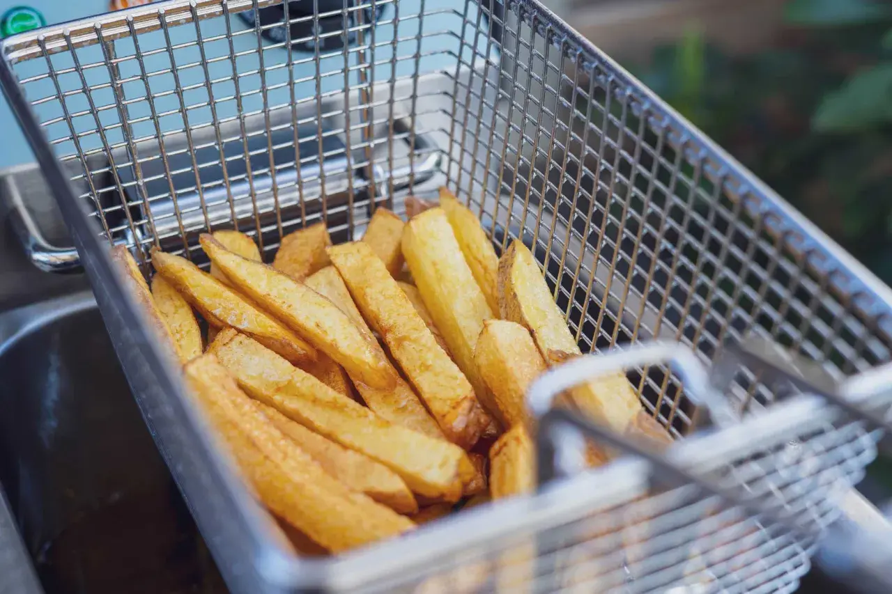 Goldgelbe Pommes in einem Frittierkorb, bereit, um sie wieder knusprig zu machen.