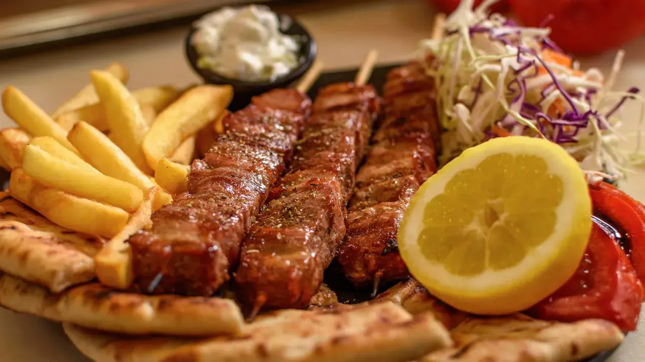 Pyszne souvlaki na patyczkach, podane z frytkami, pitą, surówką i cytryną.