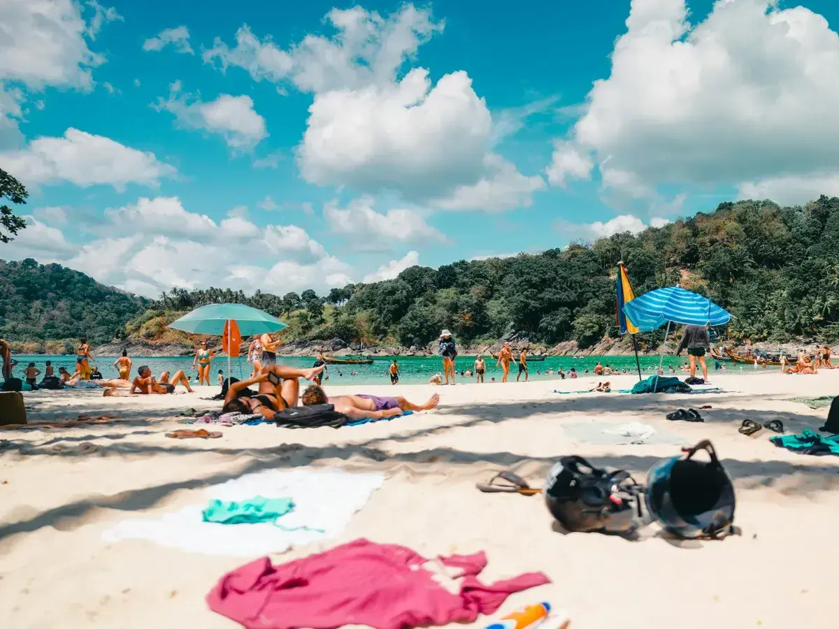 Gente disfrutando de unas **vacaciones agosto 2026** en una playa tropical, con aguas turquesas y vegetación exuberante.