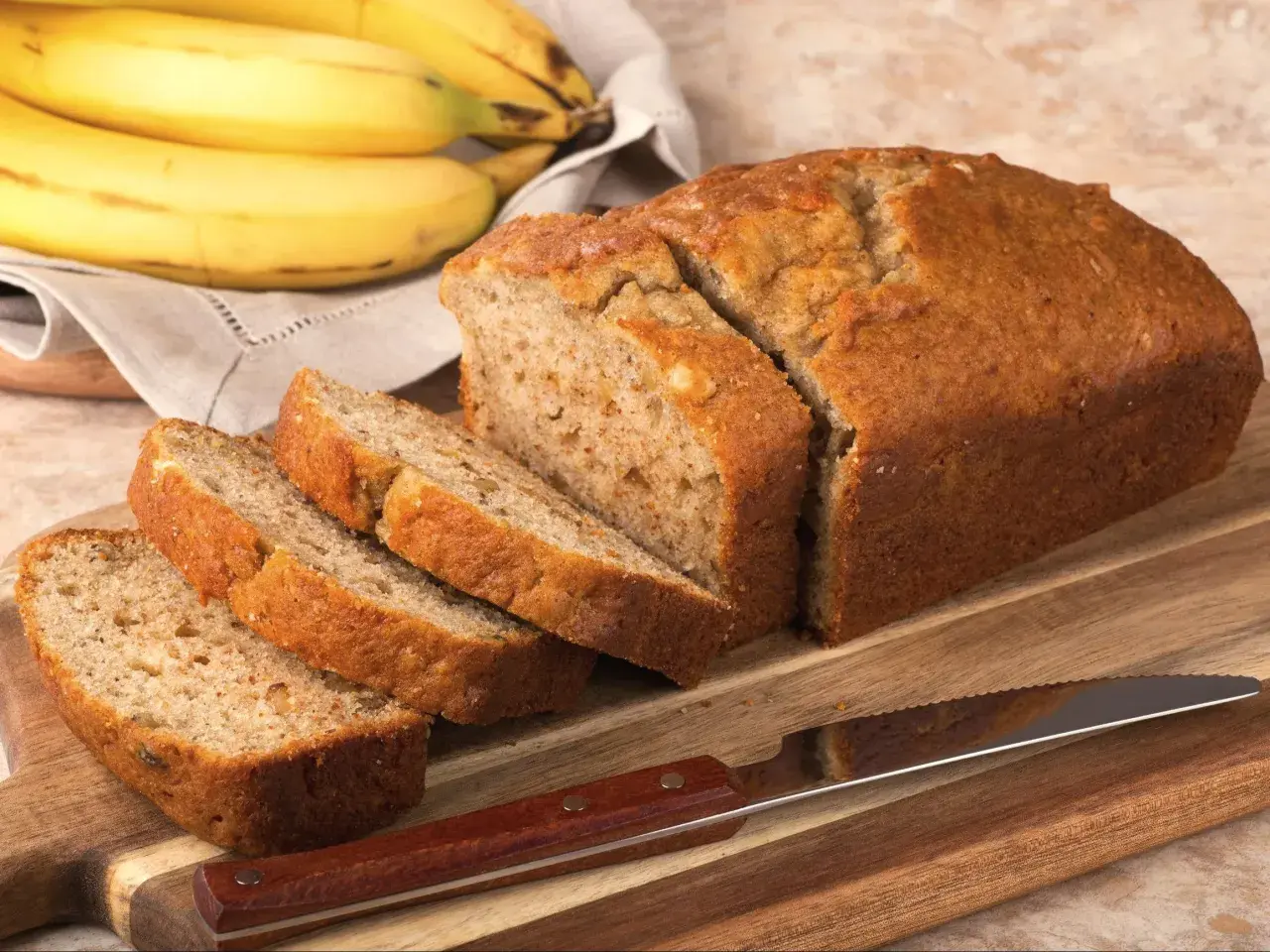Pokrojony, złocisty chlebek bananowy, obok pęk dojrzałych bananów. Idealny na najprostszy chlebek bananowy.