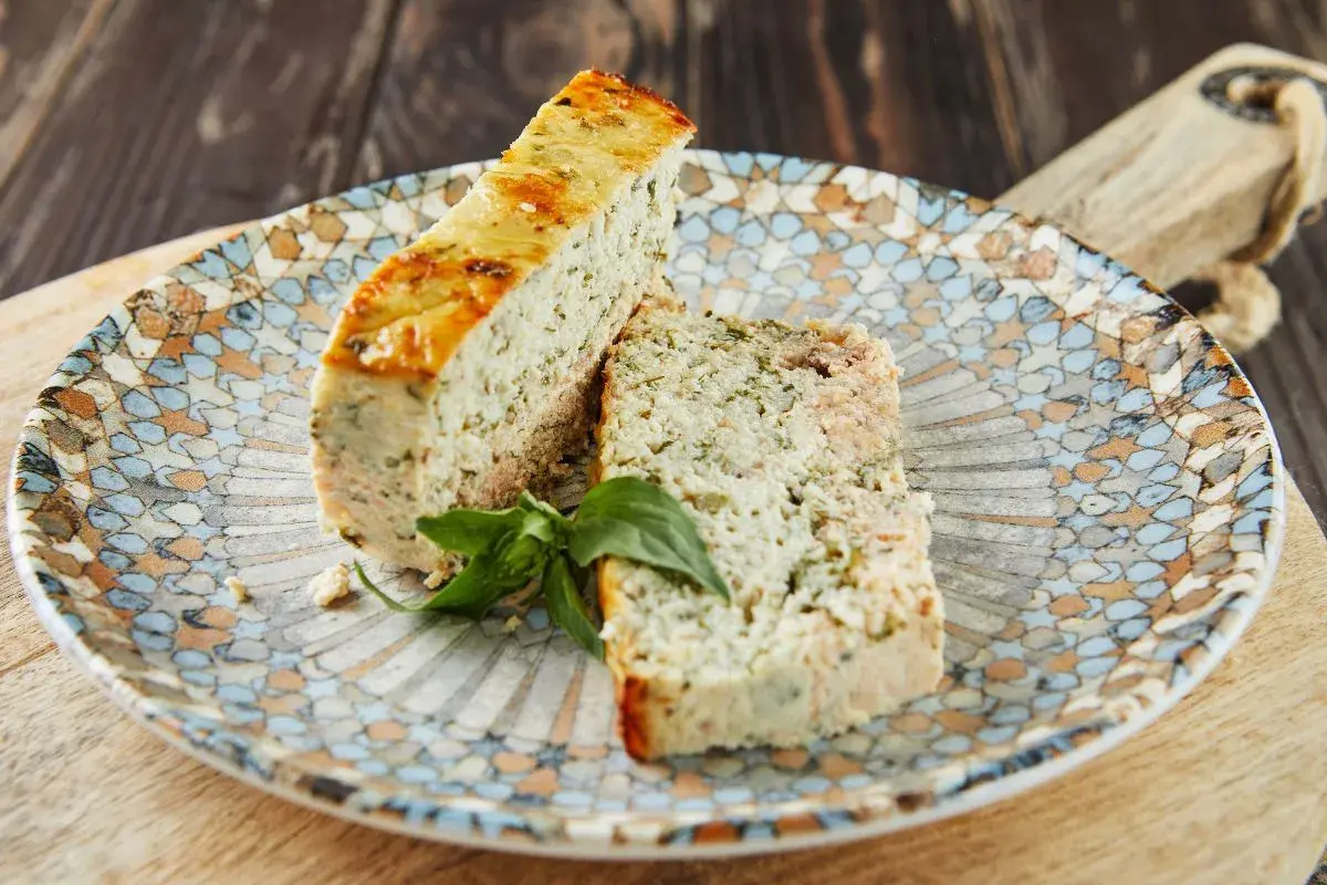 Deux tranches de terrine de poisson aux herbes, garnies d'une feuille de basilic, sur une assiette décorée.