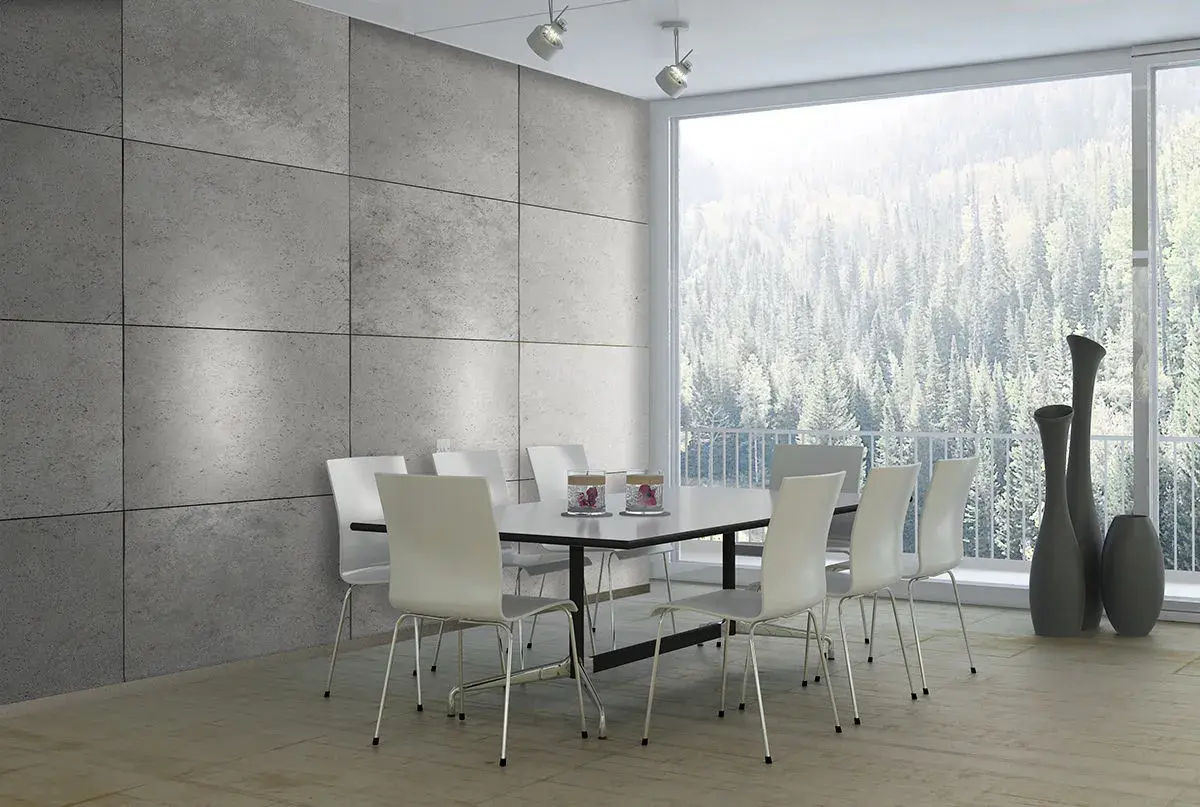 Esszimmer mit moderner Beton Optik Wandverkleidung, weißem Tisch und Stühlen, sowie einem Panoramafenster mit Blick auf einen Wald.