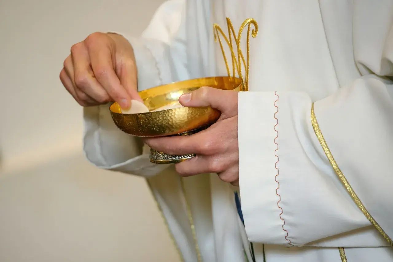 Kapłan podaje hostię z kielicha. Poważne grzechy po których nie można przystąpić do komunii wymagają spowiedzi.
