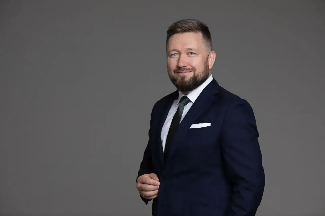 Portret mężczyzny w granatowym garniturze, białej koszuli i zielonym krawacie, z brodą i niebieskimi oczami.