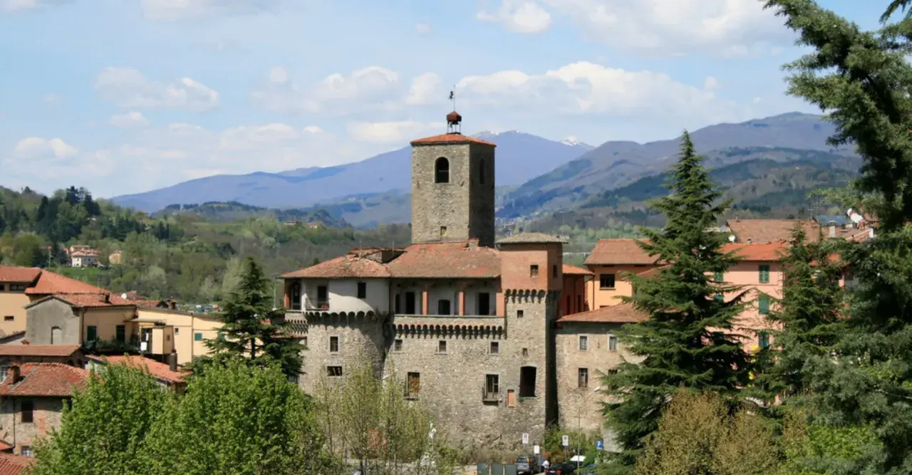 La Rocca Ariostesca domina il borgo con la sua torre imponente, circondata da colline verdi e un cielo azzurro con nuvole bianche.