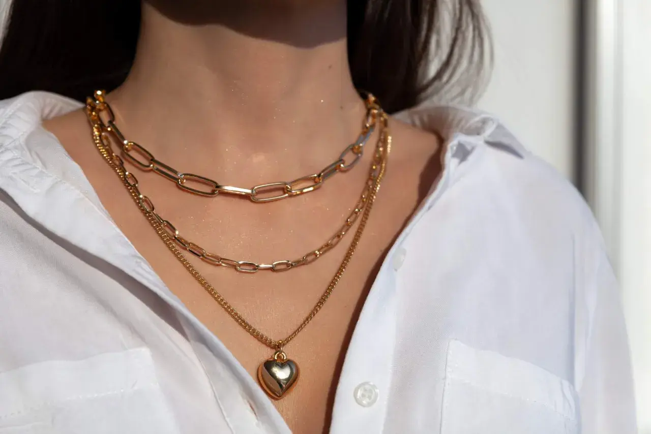 Tres collares dorados en capas, uno con un corazón, lucen perfectos con el escote de una camisa blanca.