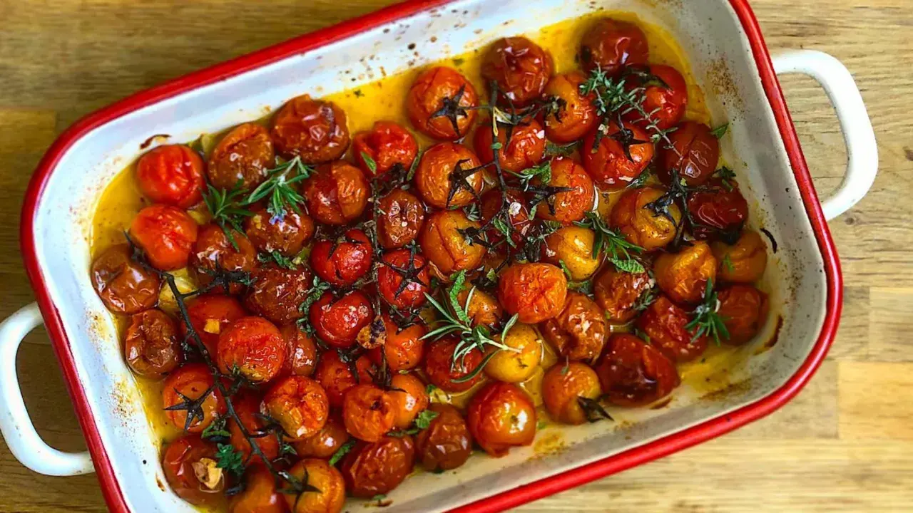 Tomates cherry confitados en aceite de oliva, con romero y tomillo, en una bandeja blanca con borde rojo.