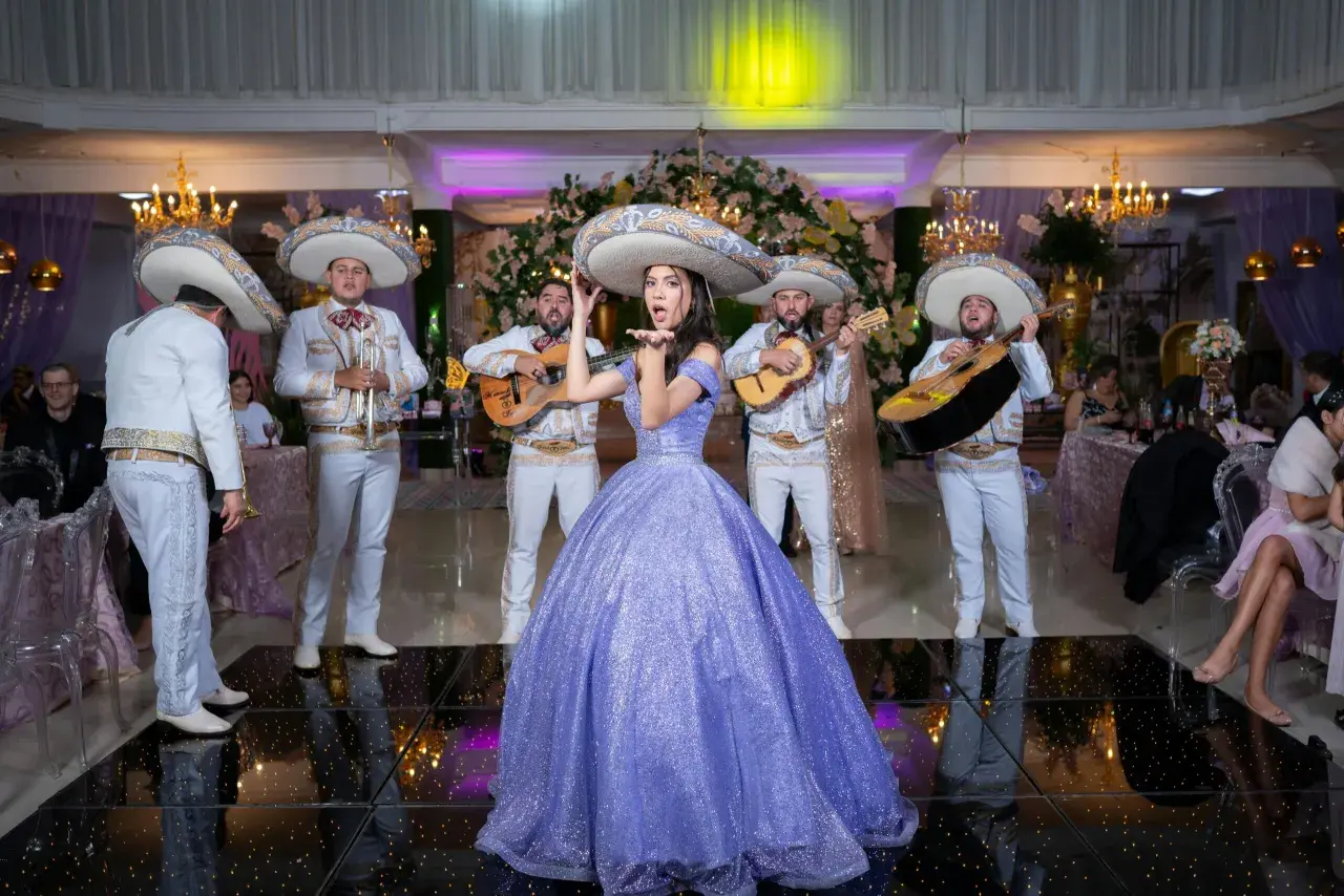 Mariachi grają przyśpiewki weselne, a młoda kobieta w fioletowej sukni posyła całusy.