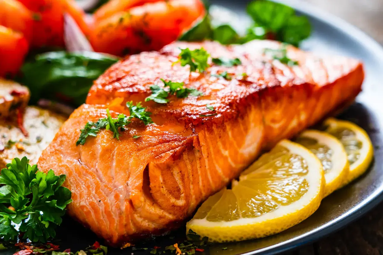 Un succulento filetto di salmone cotto alla perfezione, guarnito con prezzemolo fresco e accompagnato da spicchi di limone e pomodorini.