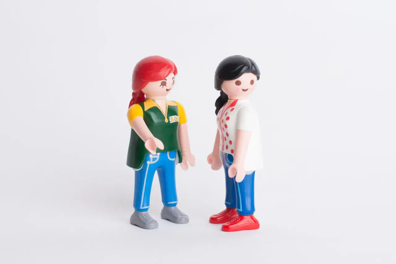Twee Playmobil-poppetjes staan tegenover elkaar. De ene met rood haar en een groen vest, de ander met zwart haar en een wit shirt. Ze lijken te praten, alsof ze elkaar vertellen dat ik hoor niet bij mijn familie.