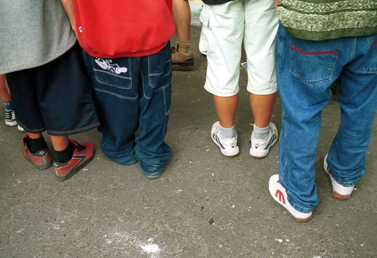 Luźne spodnie, szerokie nogawki i sportowe buty – to wszystko w stylu hip hop. Grupa młodych ludzi w luźnych ubraniach.