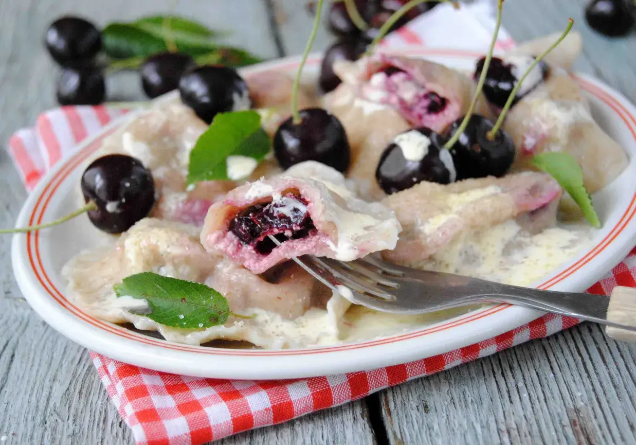 Pyszne pierogi z czereśniami, polane śmietaną, ozdobione świeżymi owocami i listkami mięty. Idealne na letni deser.