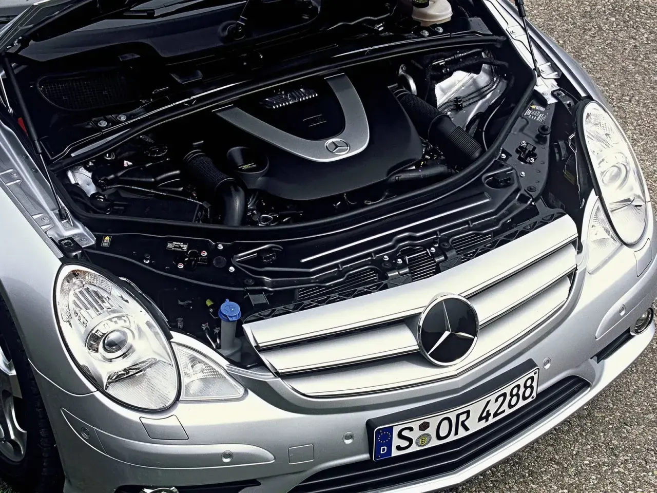 Motor de Mercedes Clase R, con capó abierto. Se aprecian componentes mecánicos y el logo de Mercedes. Posibles mercedes clase r problemas.
