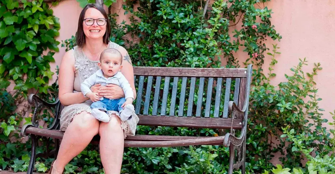 Madre sonriente abraza a su bebé en un banco. Un ejemplo de los hermosos testimonios de hijos nacidos por ovodonación.