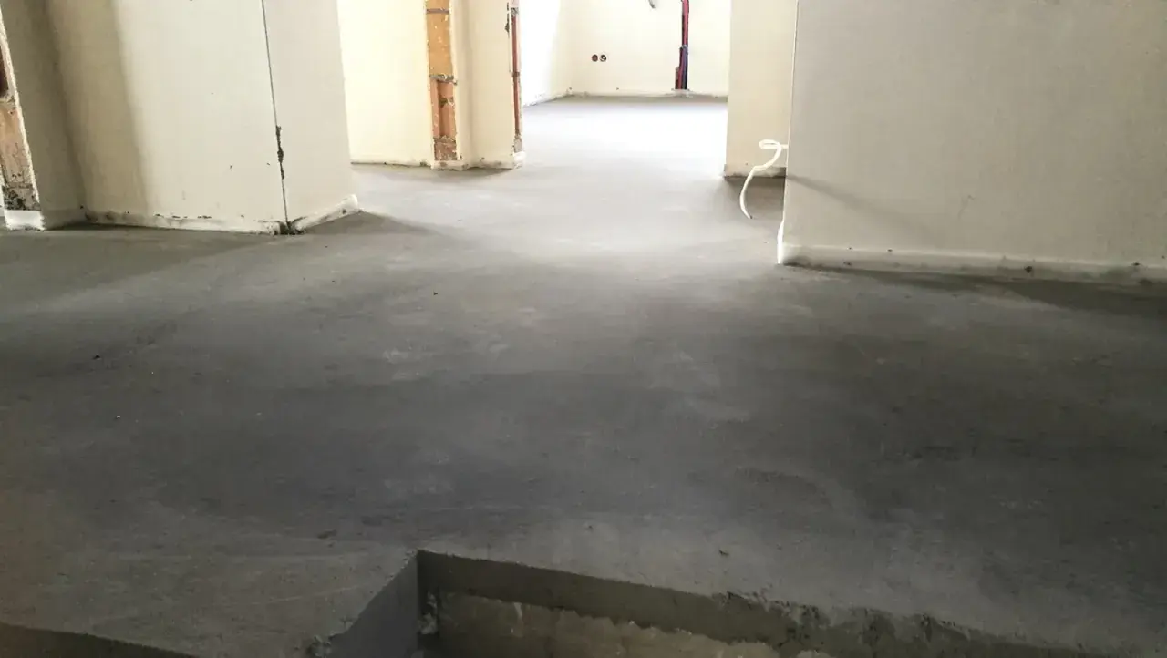 Surowy, betonowy jastrych co to? To podłoga gotowa na wykończenie. Widać fragmenty ścian i instalacji.