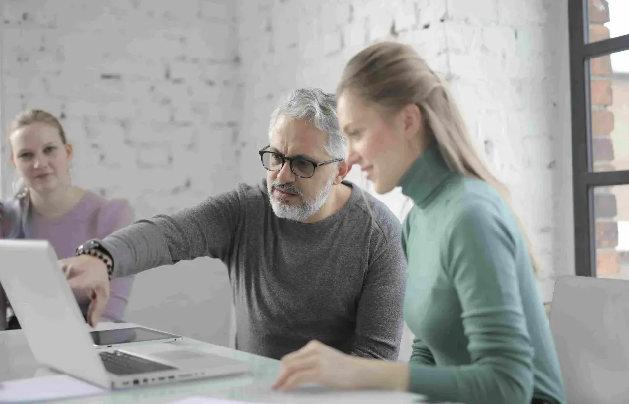 Uomo della generazione boomer spiega qualcosa su un laptop a una collega.