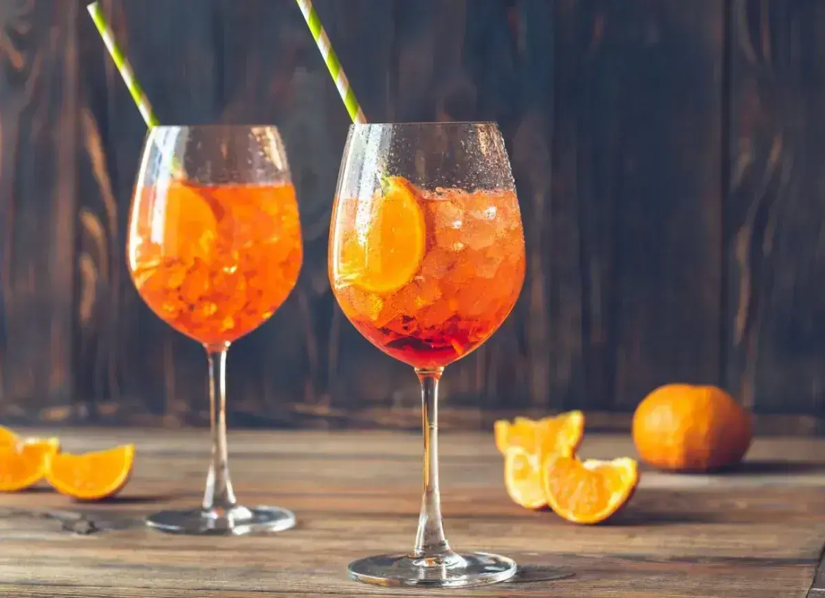 Dwa orzeźwiające aperitif spritz z plasterkami pomarańczy i słomkami, na drewnianym stole.