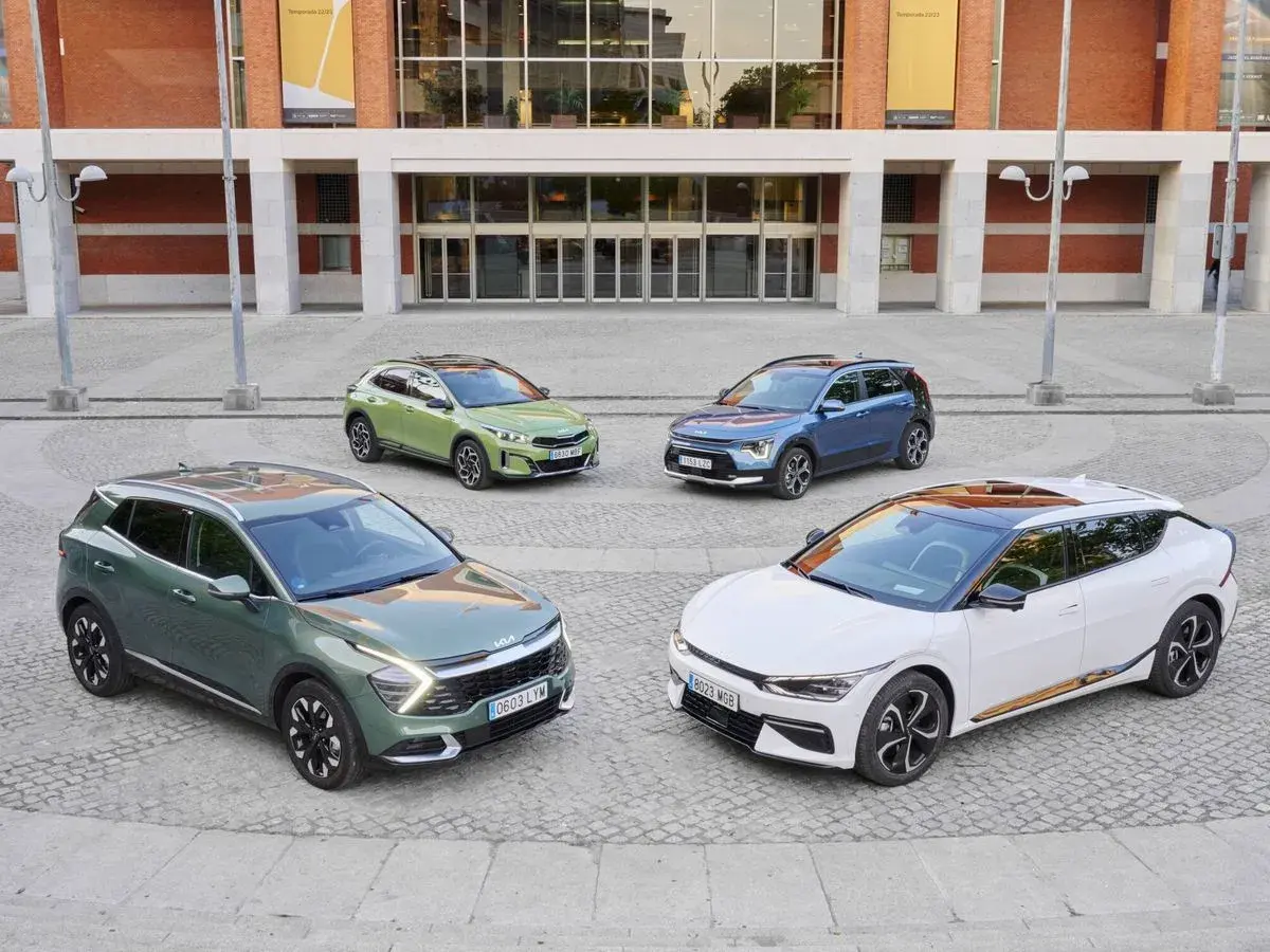 Cuatro coches Kia, dos hibridos y electricos, en tonos verde, azul y blanco, frente a un edificio moderno.