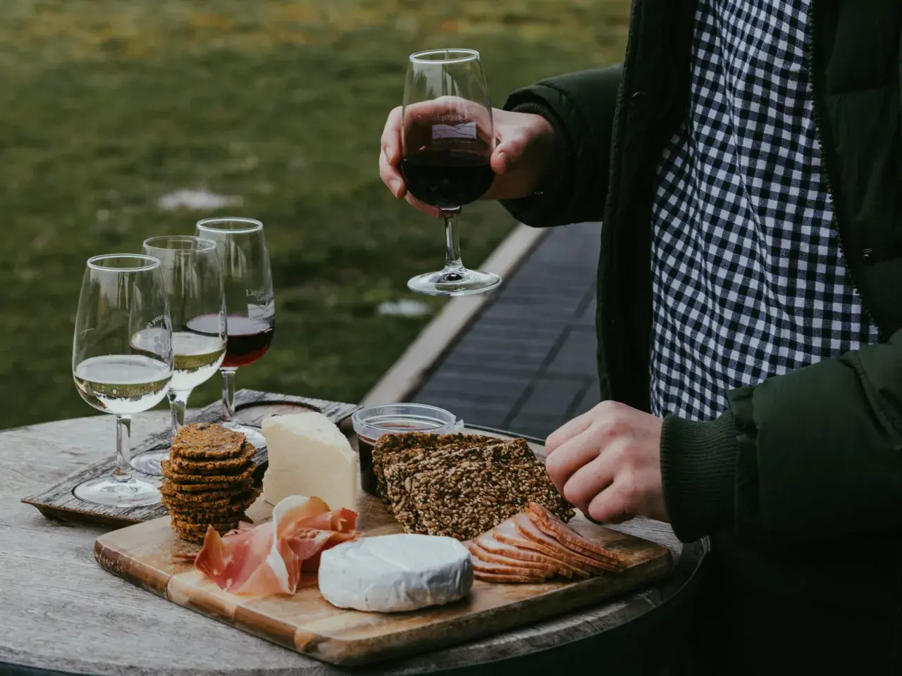 Un plateau de fromages, charcuteries et biscuits accompagne un verre de vin rouge. Une dégustation parfaite de vin et volailles en plein air.