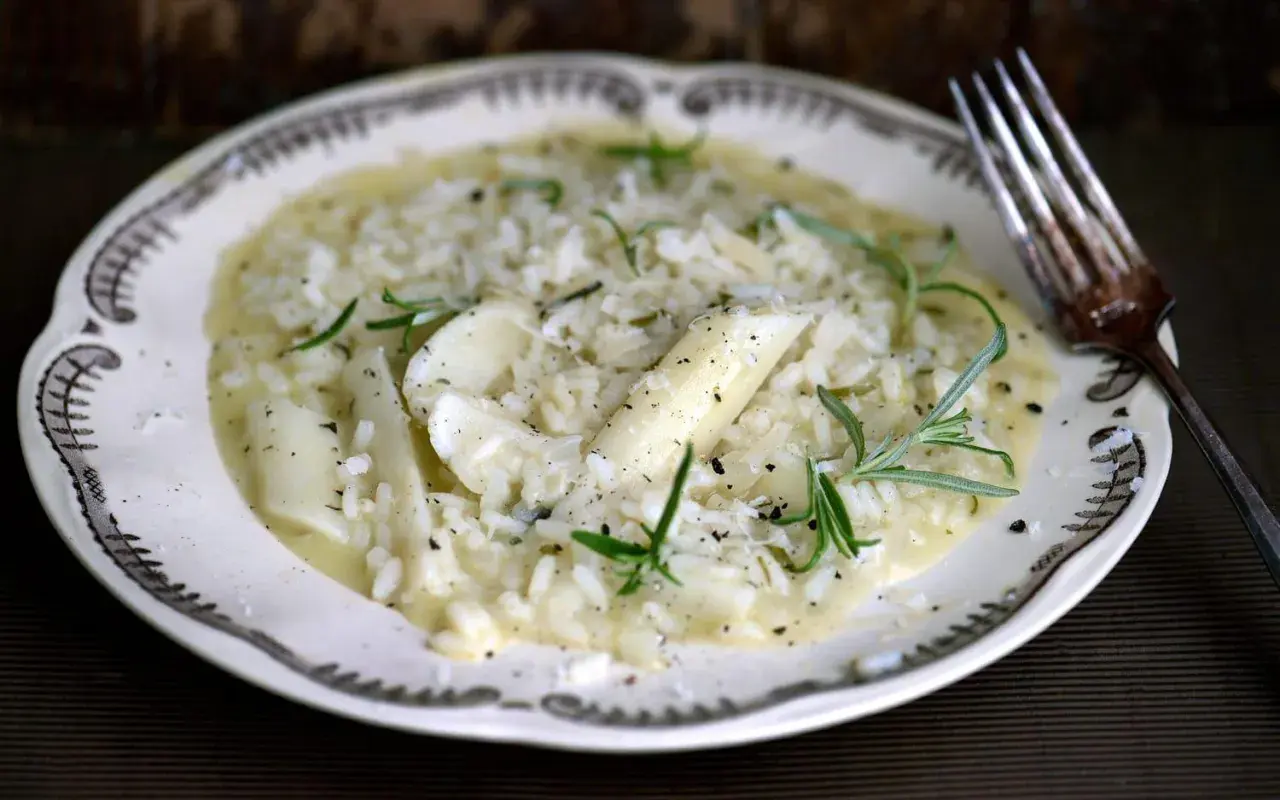 Krämig risotto med sparris och rosmarin, perfekt för ett svamprisotto recept. Serveras på en vacker tallrik med en gaffel.